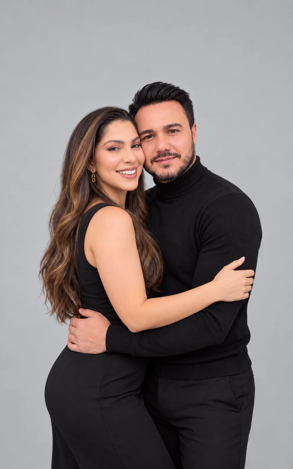 A couple embracing in coordinated black outfits against a soft gray backdrop.