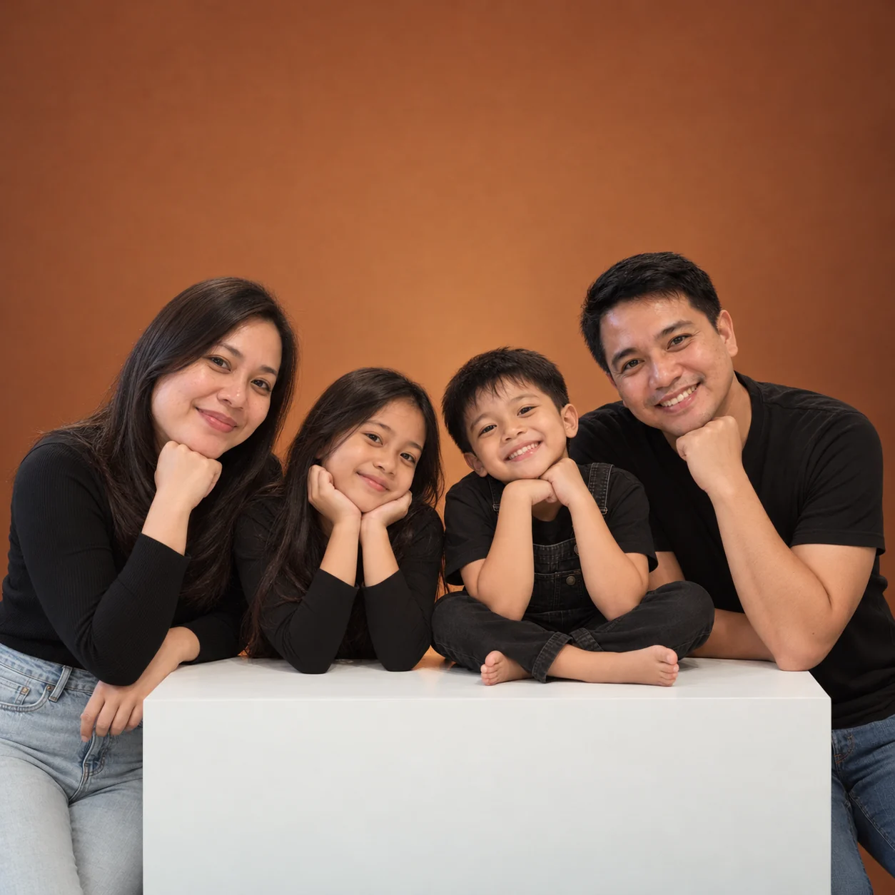 A family of four in matching black tops, leaning together against a warm orange backdrop.